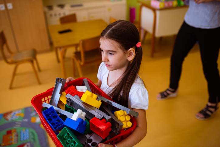 preschooler-helper Young girl helps clean up bin of toys in classroom