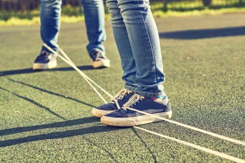 looped-to-rope Legs of two teens standing on two ropes strung on top of the pavement