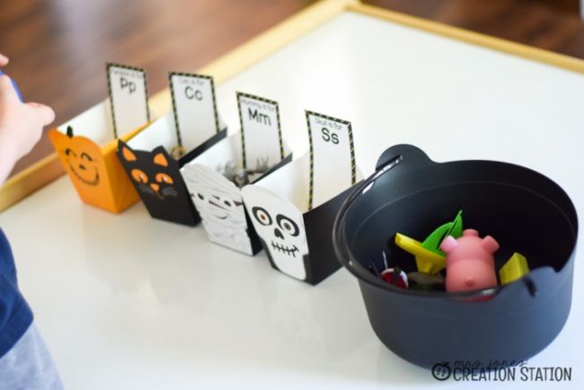 halloween-initial-sorting Plastic cauldron holding small toys next to Halloween themed boxes labeled with letters