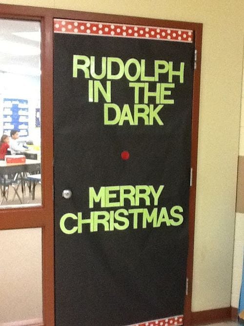 Winter Classroom Doors: Rudolph in the Dark Winter classroom doors include this one that is black and has writing that says Rudolph in the Dark. There is a red nose on the black.