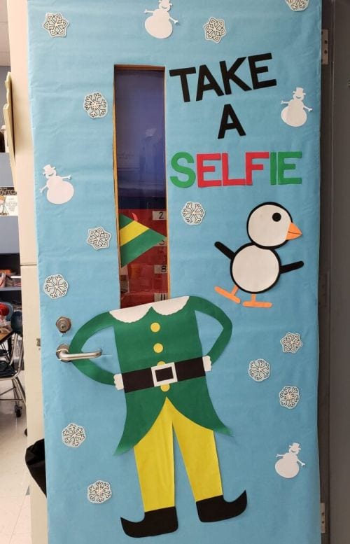Winter Classroom Doors: Elf A classroom door is decorated with the body of an elf and it says Take a Selfie.