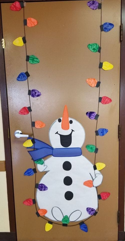 Winter Classroom Doors: Snowman Swinging Winter classroom doors include this one that shows a snowman swinging on a string of colored Christmas lights.