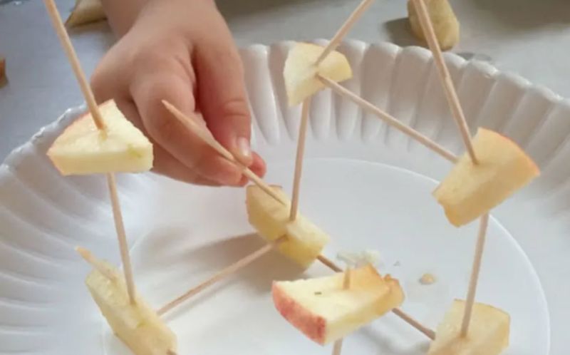 Apple Toothpick Tower STEM Challenge Child using toothpicks and pieces of apple to build a tower on a paper plate
