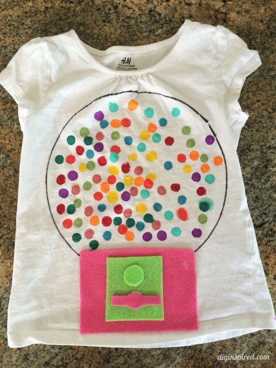 100th Day Shirt: Gumball Machine A white t-shirt has a bubble gum machine on it. There are 100 painted on dots for the bubble gum and some felt has been used to make the dispenser part of the machine (100th day of school shirt ideas)