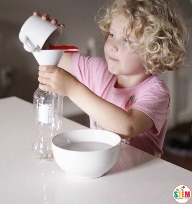 First Grade Science Experiments Young student pouring yeast through a funnel into a plastic bottle