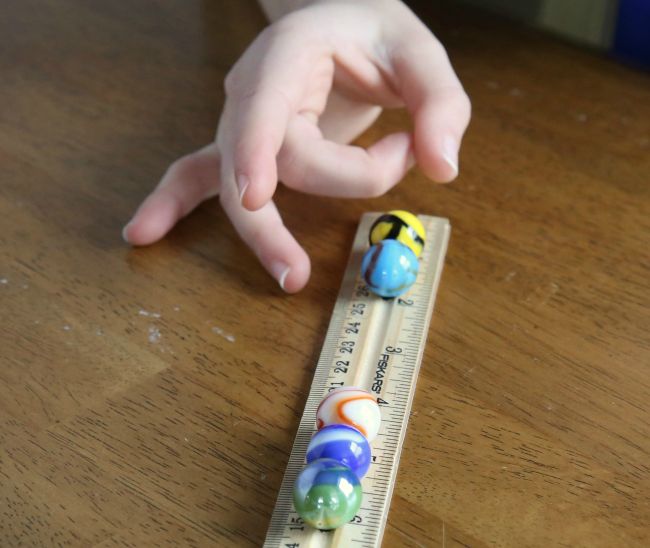 Fourth Grade Science: Marble Energy Transfer Fourth grade science student flicking a marble along the ridge in a ruler