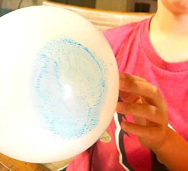Kindergarten Science Activities Fingerprints Child holding up a balloon with an enlarged blue fingerprint on it (Kindergarten Science Activities)