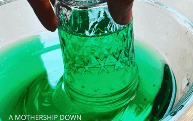 Kindergarten Science Activities Suspend Water Student's hand lifting an upside-down jar from a bowl of green water, with water kept inside the jar by air pressure