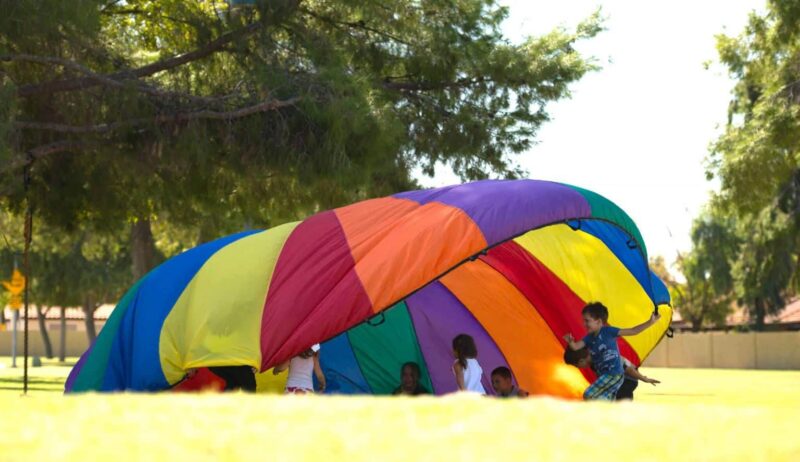 parachute-games kids playing under a parachute for a fun friday activity