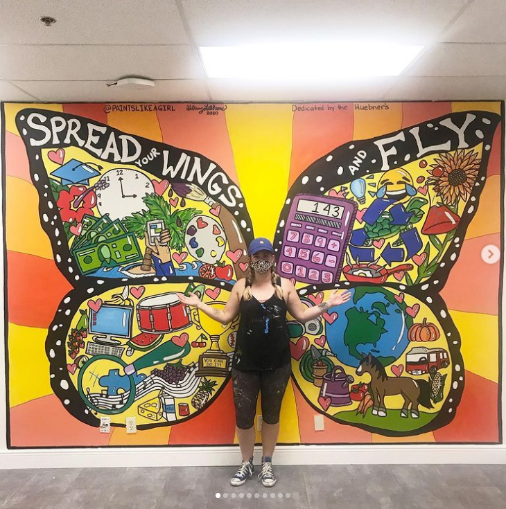 spread-your-wings-mural teacher standing in front of a mural of butterfly wings