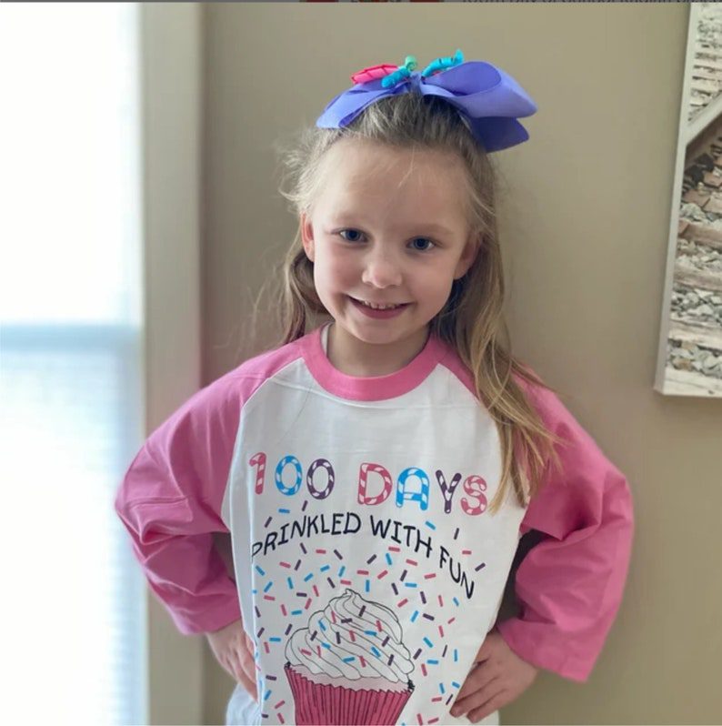 100th Day Shirt: Sprinkles A little girl wears a shirt with pink sleeves that has a cupcake on it and says 100 Days Sprinkled with Fun.