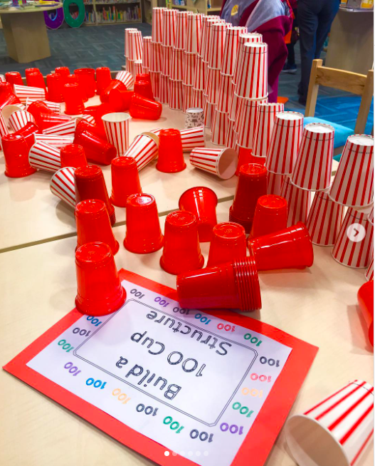 100-red-cups Red plastic cups on a table are set beside a label that says