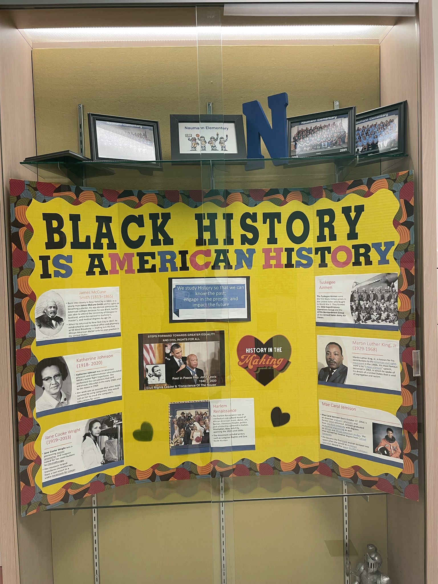 Black History Month Bulletin Board – American History A bright yellow board has writing across it that says Black History is American History. It has photos and descriptions of events and people from Black history. (black history month bulletin board)