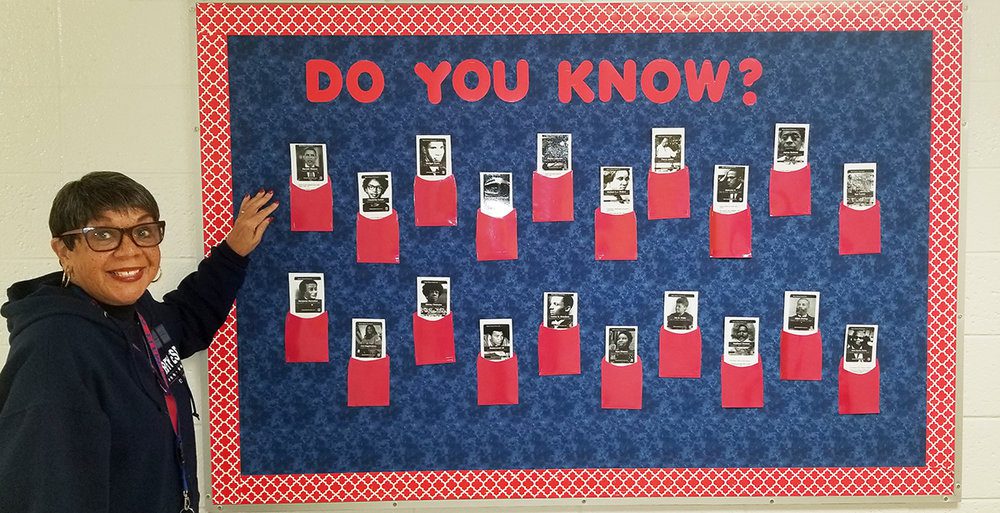 Black History Month Bulletin Board – GCPS Photo Gallery A woman stands in front of a bulletin board that says Do you know? across the top. It has photos of famous Black people on it with flaps to lift (black history month bulletin board)