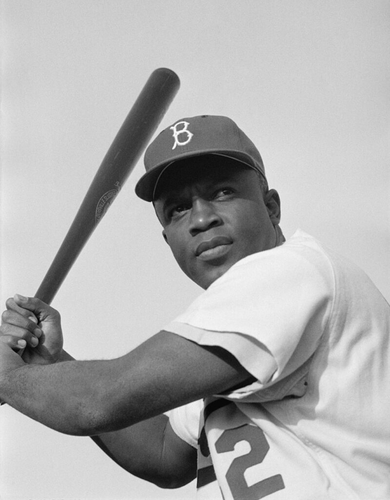 35 Famous Black Americans Everyone Should Know Black and white photo of Jackie Robinson swinging a bat