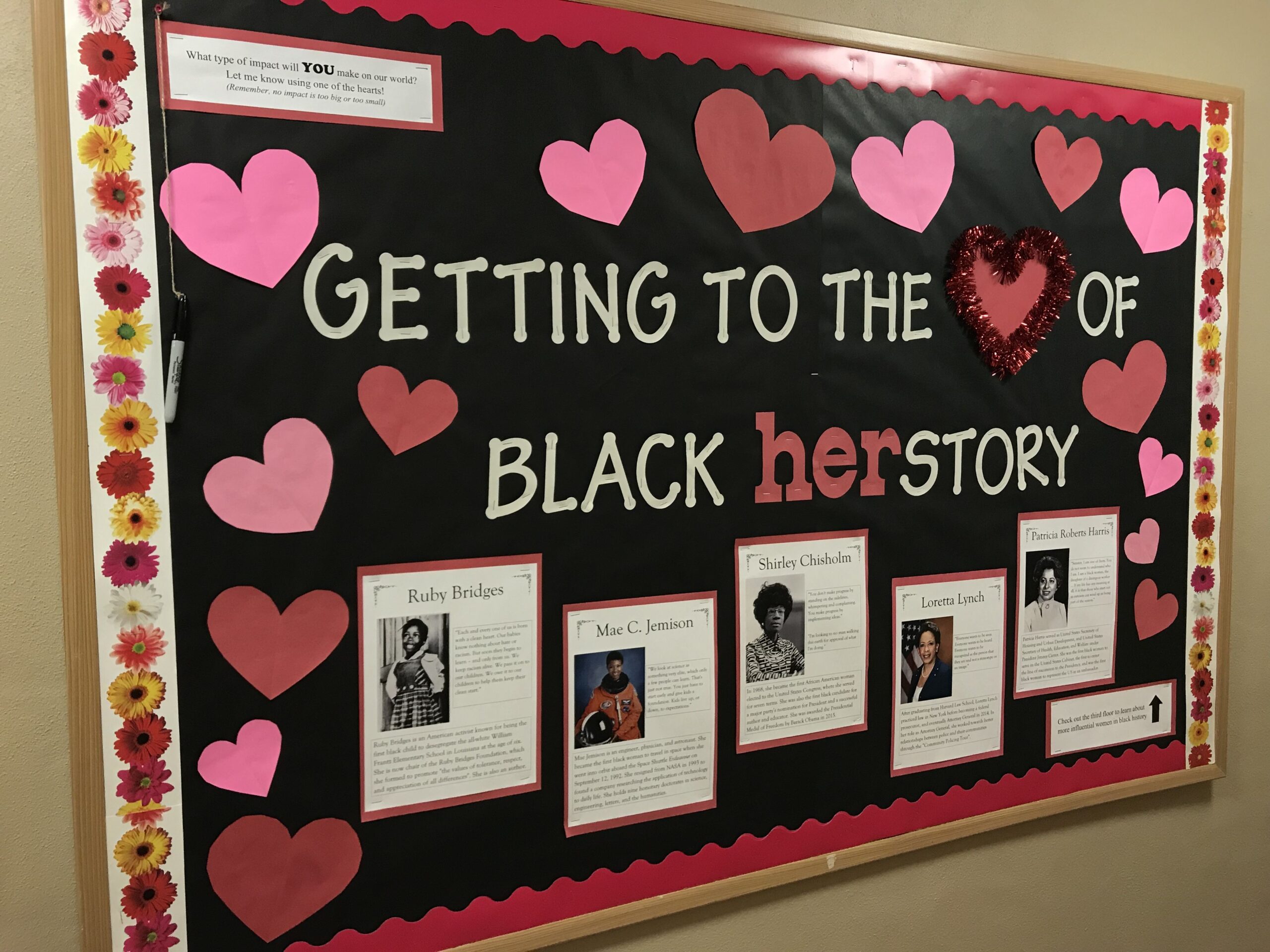 Black History Bulletin Board – Herstory A black bulletin board says Getting to the heart of Black herstory. There are pink and red hearts on the border and photos and descriptions of famous Black women.