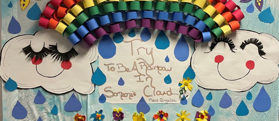 Black History Month Bulletin Board – Rainbow Text reads Try to be a rainbow in someone's cloud - maya angelou. There is a rainbow made up of different colored construction paper rolled into small tubes.