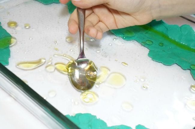 Sixth Grade Science Oil Spill Clean Up Sixth grade science student using a spoon to try to catch a puddle of oil floating on water