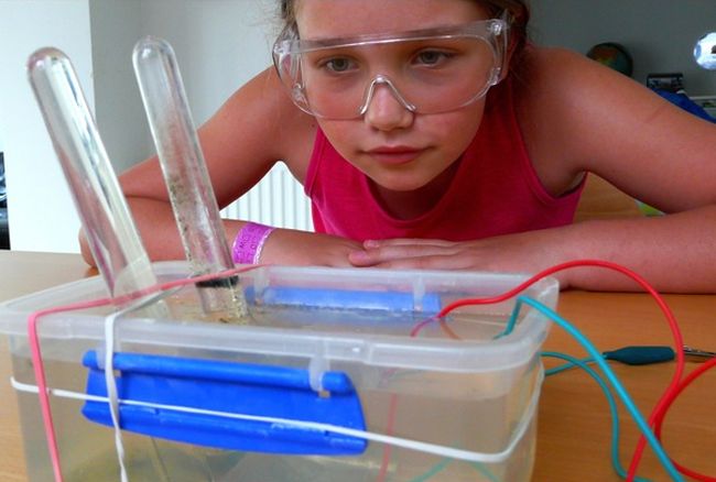 8th Grade Science Electrolysis Navigating by Joy Eighth grade girl wearing goggles, looking at a container of water with test tubes and electric wires