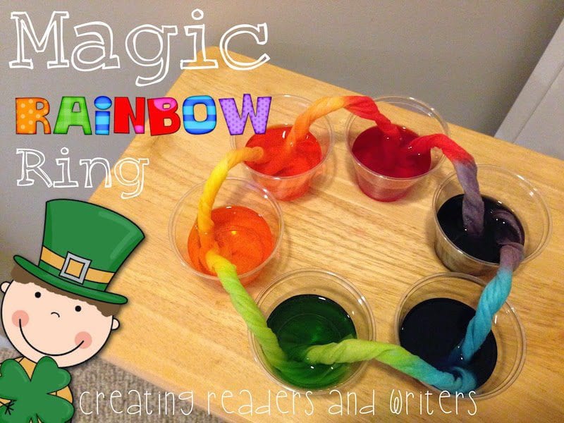 Magic Rainbow Ring rolled up piece of fabric is dipped into plastic cups filled with water and food coloring on a desk, as an example of St. Patrick's Day activities