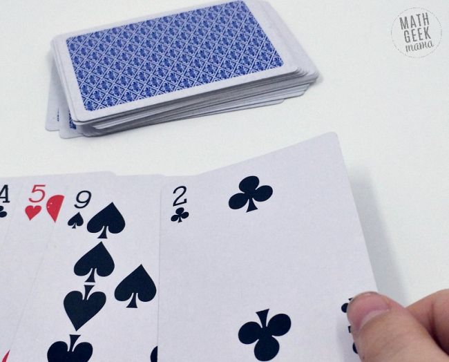 Pi Day Cards Math Geek Mama A hand holding a two of clubs as part of a set of cards turned face up next to a stack of cards piled up face down
