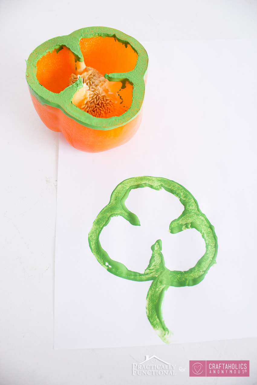 Use-A-Bell-Pepper-As-A-Shamrock-Stamp-5 an orange bell pepper rimmed with green paint and a print of a shamrock on a piece of white paper, as an example of St. Patrick's Day activities