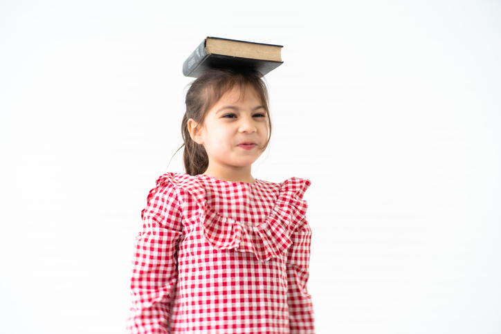 Girl with Book on Head A dark haired little girl is shown from the waist up with a book balanced on her head in this example of minute to win it games.