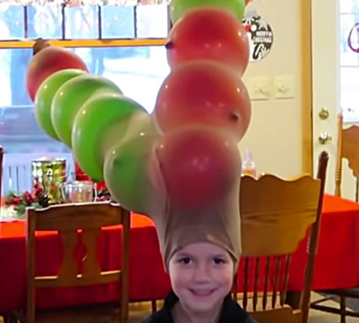 Balloon Antlers A little child is shown from the neck up. He is wearing a pair of nylons on his head that have been filled with balloons to look like antlers in this example of minute to win it games.