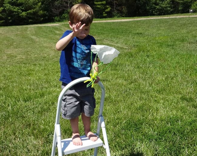 Outside Science Inspiration Laboratories Child standing on a stepladder dropping a toy attached to a paper parachute