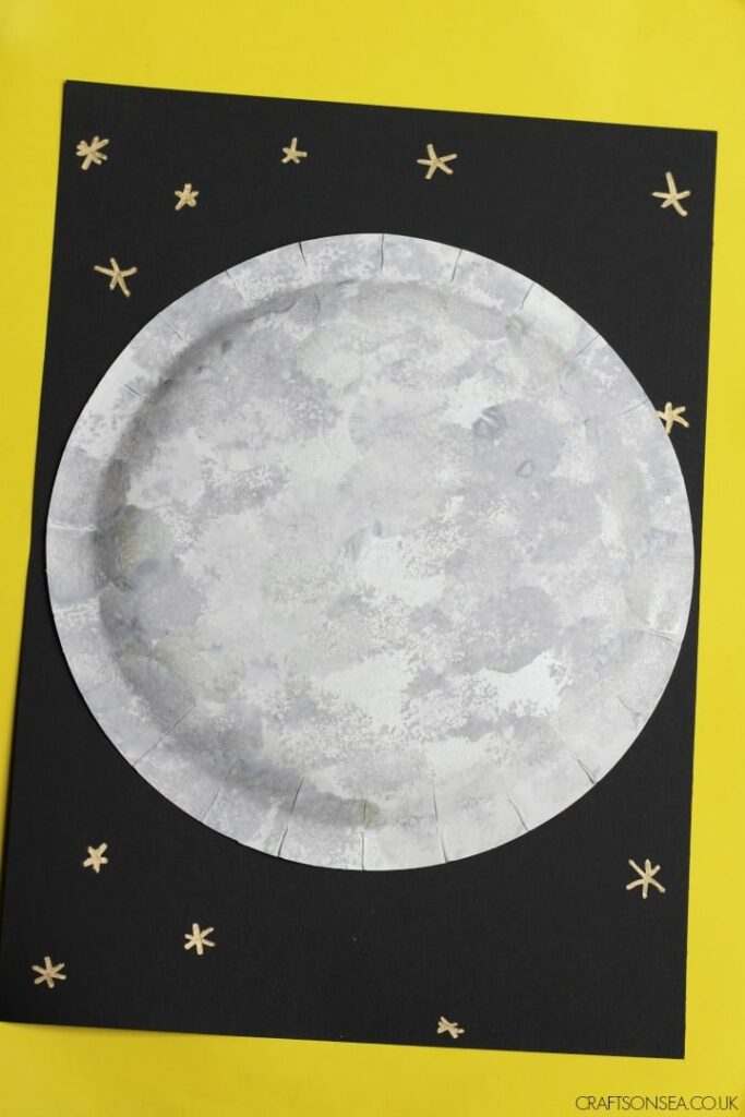 Pom-Pom-Printed-Moon A black background has stars and a large moon made from a paper plate.