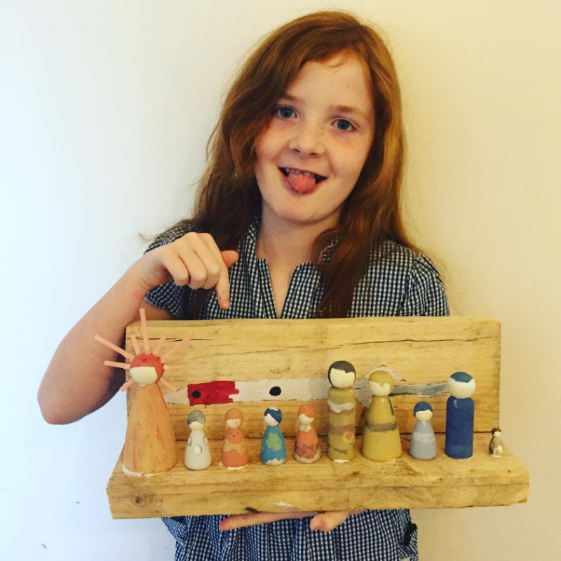 Solar-System-Peg-Dolls A little girl is holding a wooden box that has 9 peg dolls designed to look like the sun and planets.