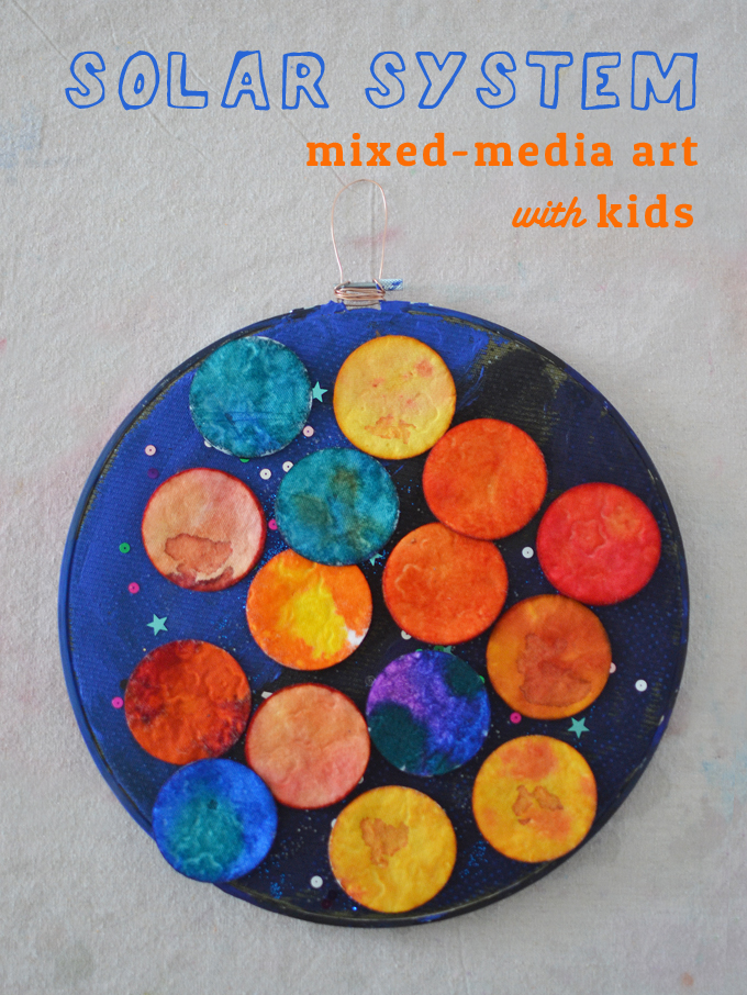 solarsystemmixedmedia A blue embroidery hoop has different round cotton pads on it that are painted to look like planets.
