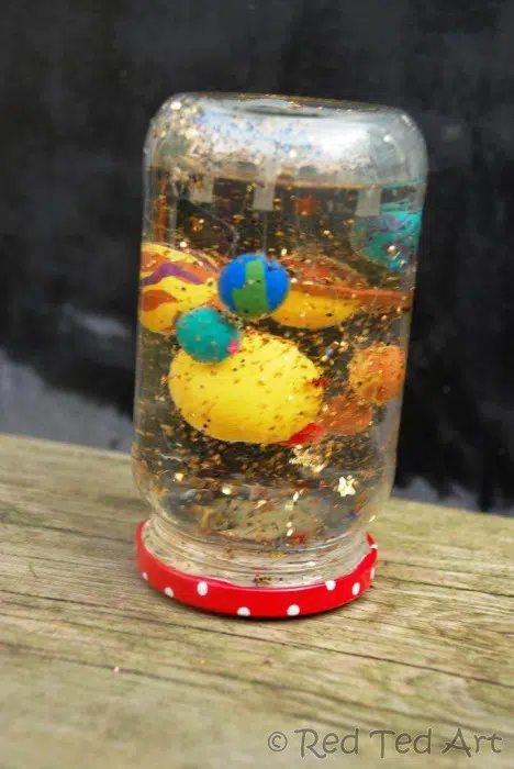 spacesnowglobe A snow globe made from an upside down jar has glitter and planets inside it (solar system planets)