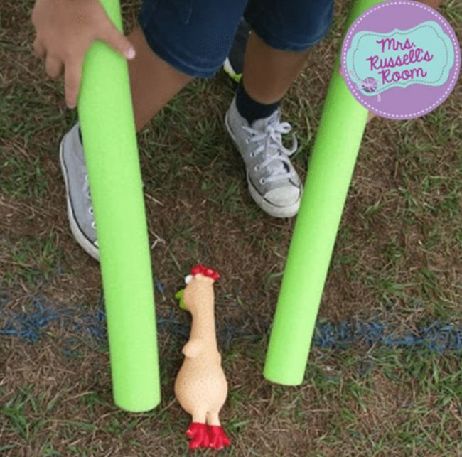 Child using pool noodles to pick up a rubber chicken