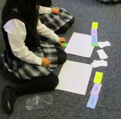 pick-a-sentence A girl in a school uniform sits on the carpeted classroom floor playing a grammar game