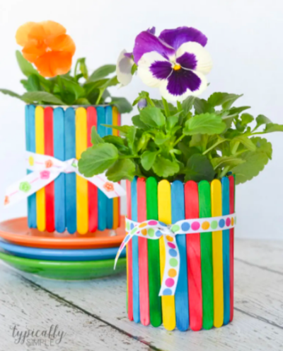 craft-stick-flower-pot A flower pot made from colorful craft sticks glued around a tin can, with colorful flower planted inside as an example of summer crafts for kids