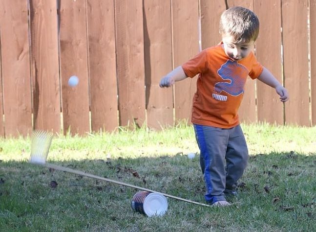 DIY Catapult Child jumping on one side of a wooden board propped over a can, sending a ping pong ball on the other side flying