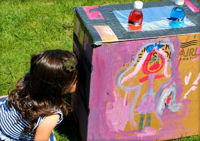 Light Box Child peering into a painted cardboard box turned into a light box with colored water in bottles