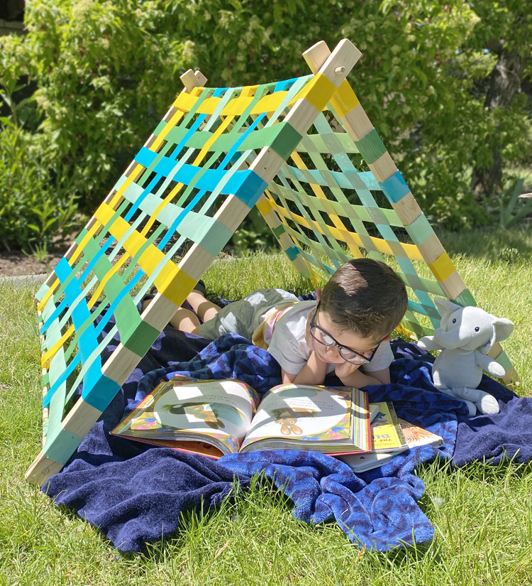 duck-tape-tent-diy A boy reading reclines under a tent made from a wood frame and duct tape walls as an example of summer crafts for kids