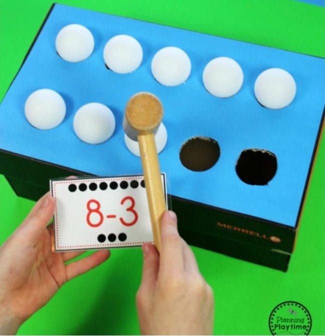 whack-a-ball shoebox with hole and balls and a hand tapping one of the balls