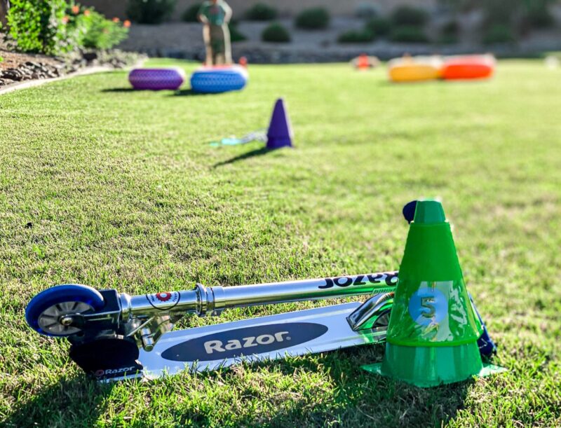 Razor_Obstacle_Course Some inflatable tires and cones are laid out in the background and in the foreground a folded Razor scooter is seen beside a green cone in this example of obstacle courses for kids.