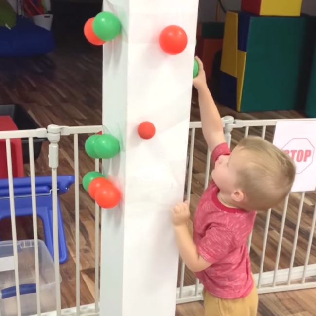 DIY Obstacle Courses for Kids: Apple Picking Toddler stretching up to pick a plastic ball off a white column
