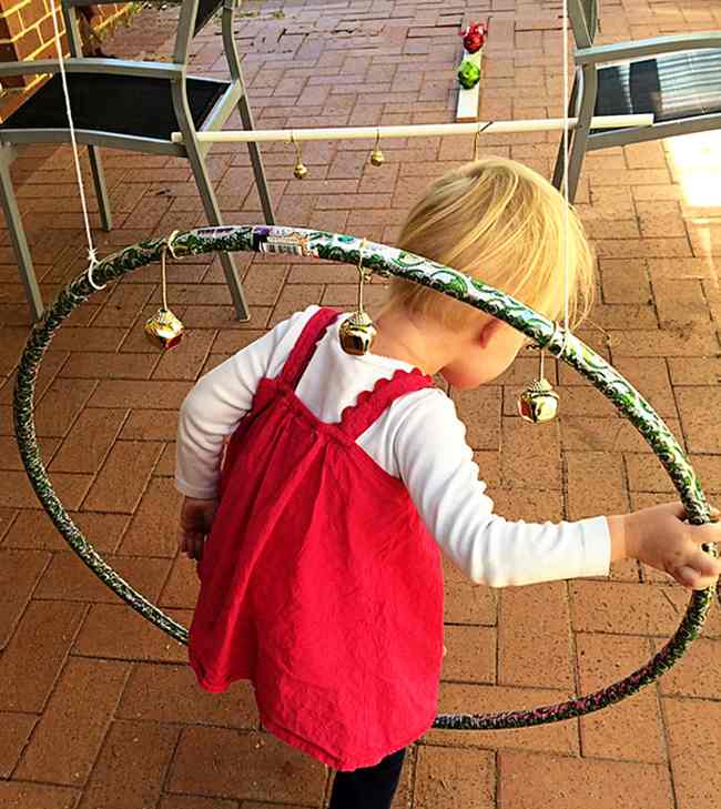 DIY Obstacle Courses for Kids: Bells Toddler climbing through a hula hoop with jingle bells attached to it in this example of obstacle courses for kids