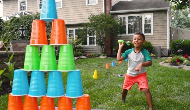 DIY Obstacle Courses for Kids: NERF Child throwing a NERF football at a stack of colorful plastic cups
