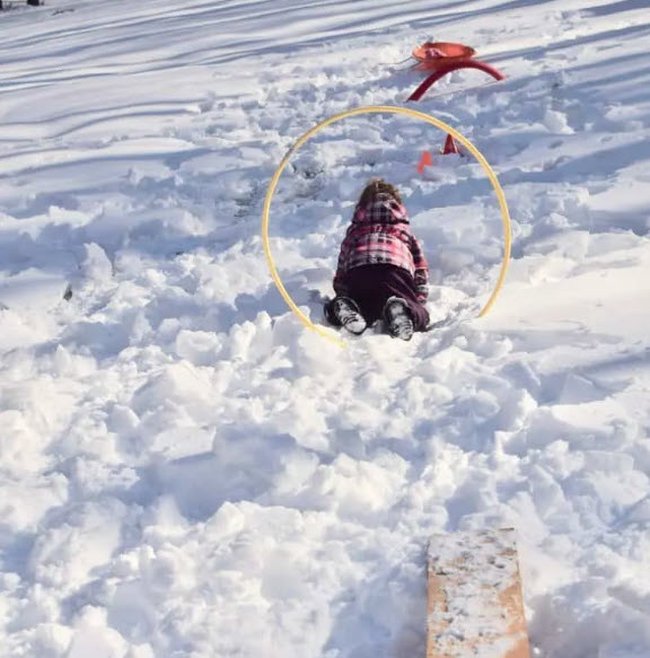 DIY Obstacle Courses for Kids: Snow Child climbing through a hoop stuck into a pile or snow in this example of obstacle courses for kids