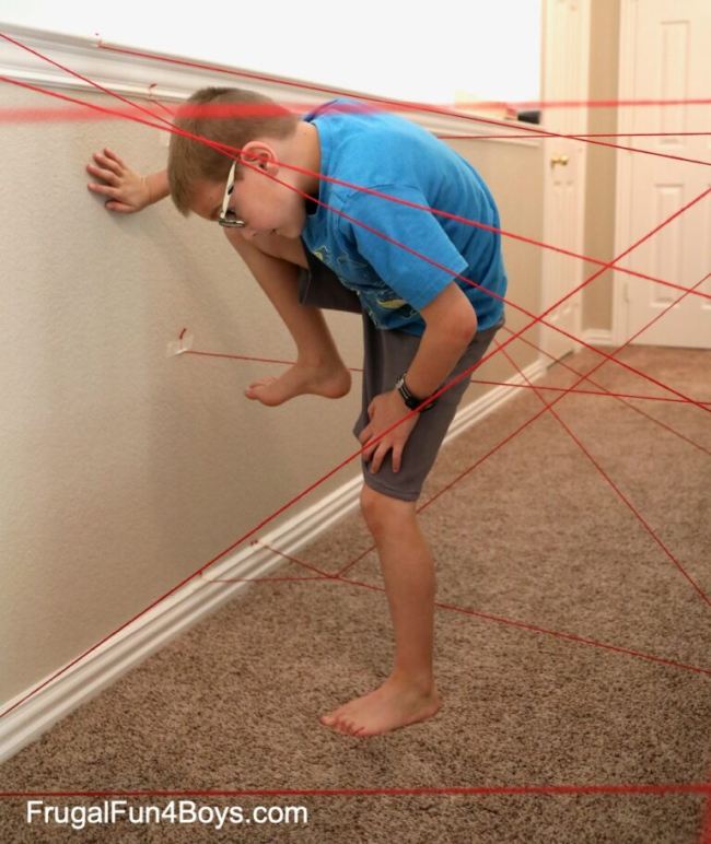 DIY Obstacle Courses for Kids: Spy Training Child climbing over and under strings taped to a wall, trying not to touch them in this example of obstacle courses for kids