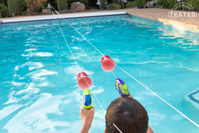 DIY Obstacle Courses for Kids: Squirt Guns Kids using squirt guns to propel plastic cups along strings strung over a swimming pool