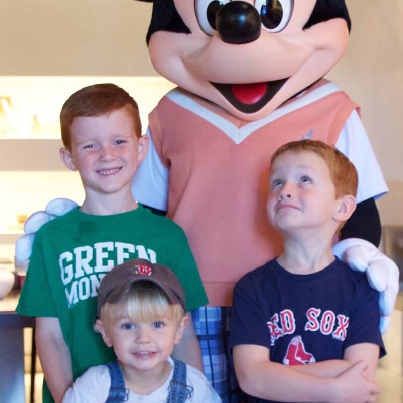 Three kids posing for a photo with Mickey Mouse.