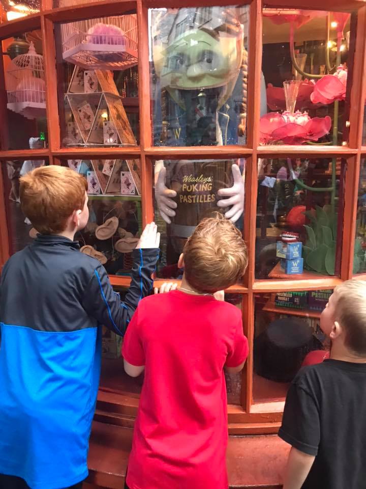 Three boys looking through a store window at Harry Potter World.