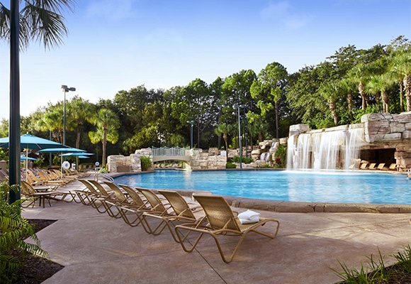 Resort pool with deck chairs next to it and trees in the background